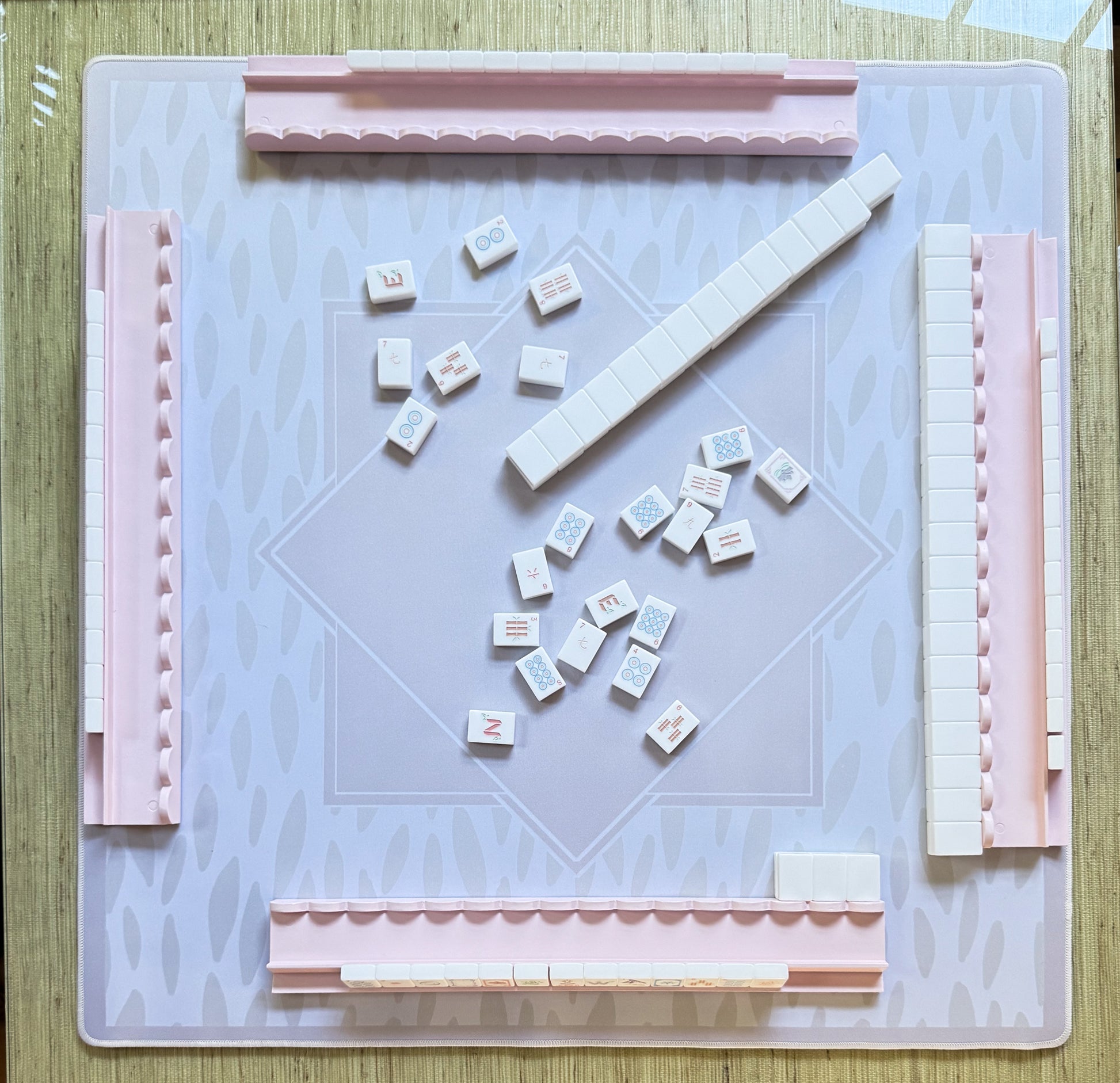Mahjong game setup with tiles and wooden mahjong rack  on a light beige and white pattern neoprene mat